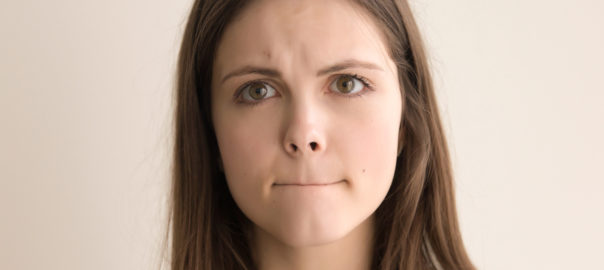 Headshot portrait of indecisive young woman. Beautiful teen girl with pursed lips and worried facial expression looking at camera. Nervous tension, bad feelings and stress. Close up. Front view
