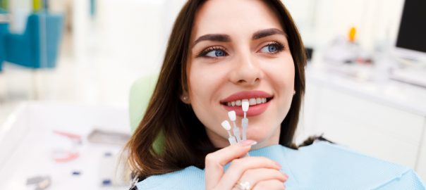 Woman smiling in dentist chair, holding dental veneers