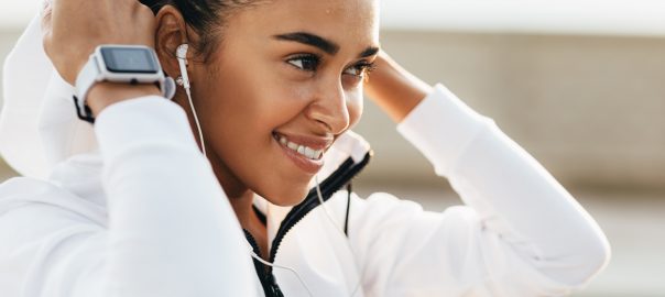 Side angle woman smiling apple watch on wrist, earpods in ears, pulling up hood