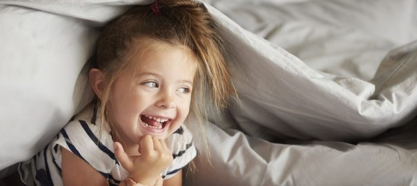 Cheerful girl hiding under the sheets
